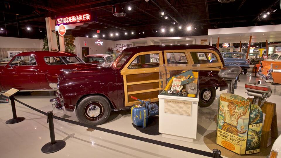 Carros antigos em exposição, incluindo um carro vermelho e uma van marrom. Também se veem equipamentos de pesca e caixas de iscas.