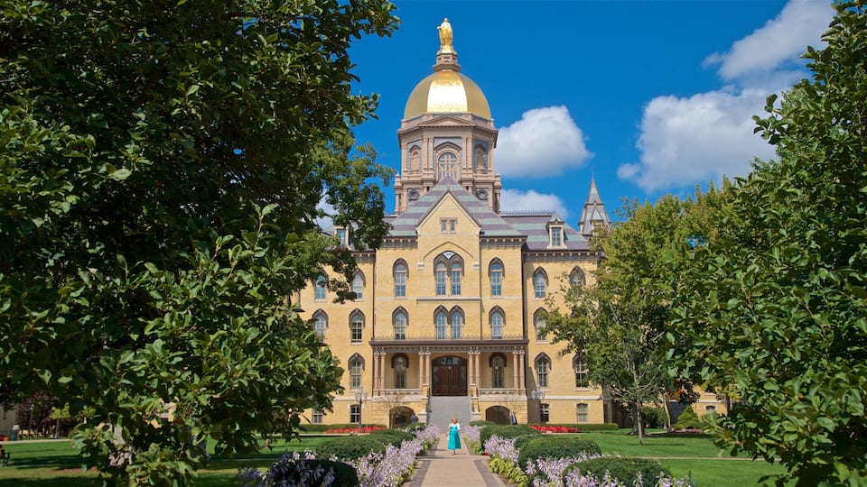 A large yellow building with a golden dome and a statue on top, surrounded by trees and a well-maintained garden.