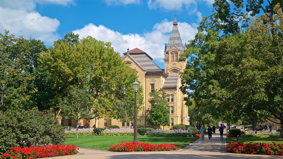 A historic building with a prominent tower, surrounded by lush greenery and vibrant flower beds.