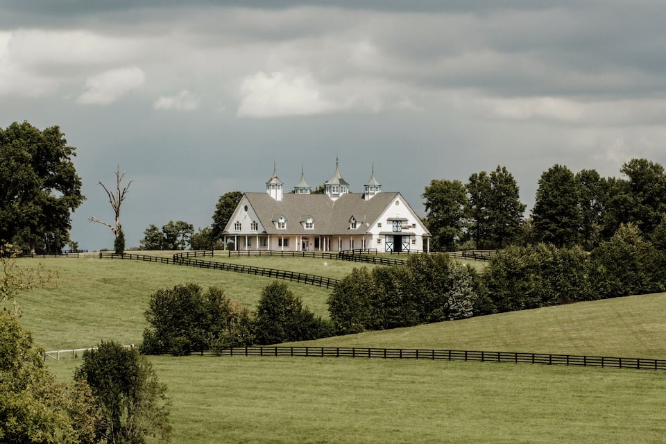 A large white house with multiple towers on a grassy hill under a cloudy sky.
