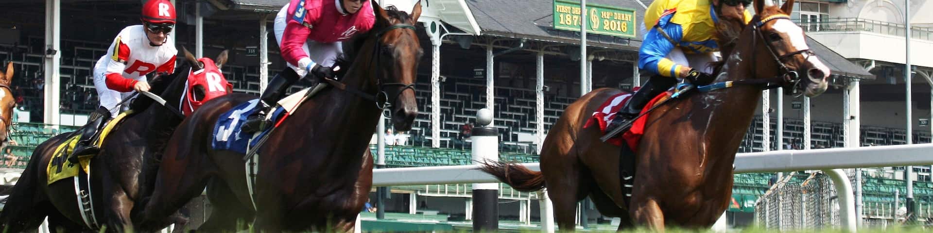 Jockeys on horses racing at a track with distinctive white towers in the background.