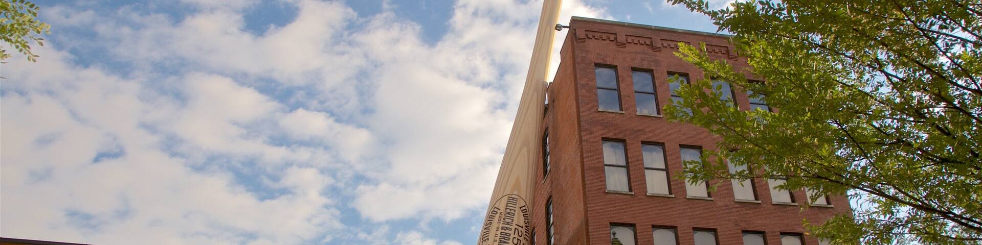 A tall wooden baseball bat leaning against a brick building with a sign reading "Hillerich & Brassler Co."