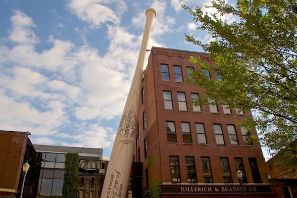 A tall wooden baseball bat leaning against a brick building with a sign reading "Hillerich & Brassler Co."