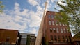 A tall wooden baseball bat leaning against a brick building with a sign reading "Hillerich & Brassler Co."