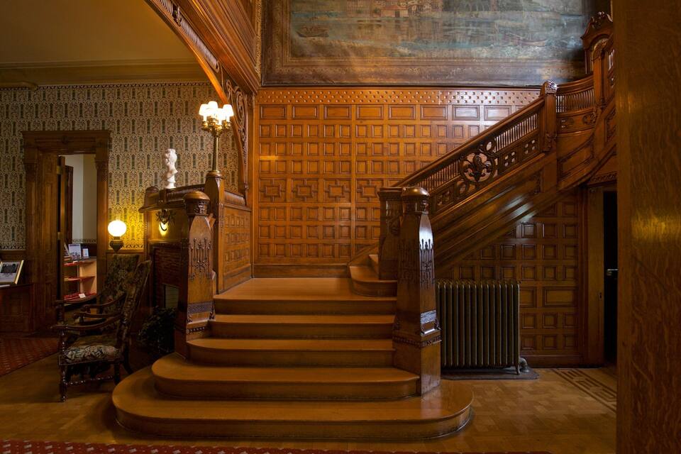 Una gran escalera con elaborados trabajos en madera y un papel tapiz decorado.