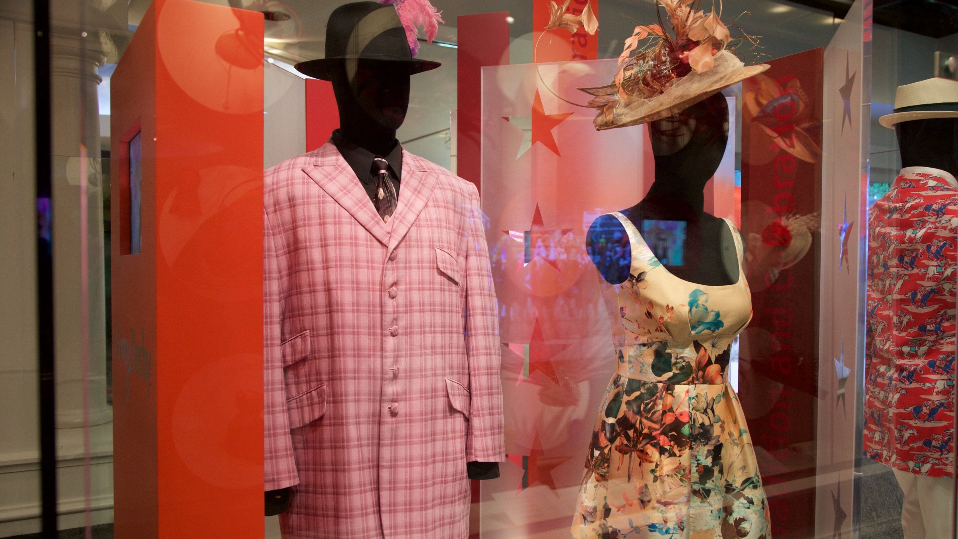 Mannequins in a store window displaying a pink plaid suit and a floral dress.