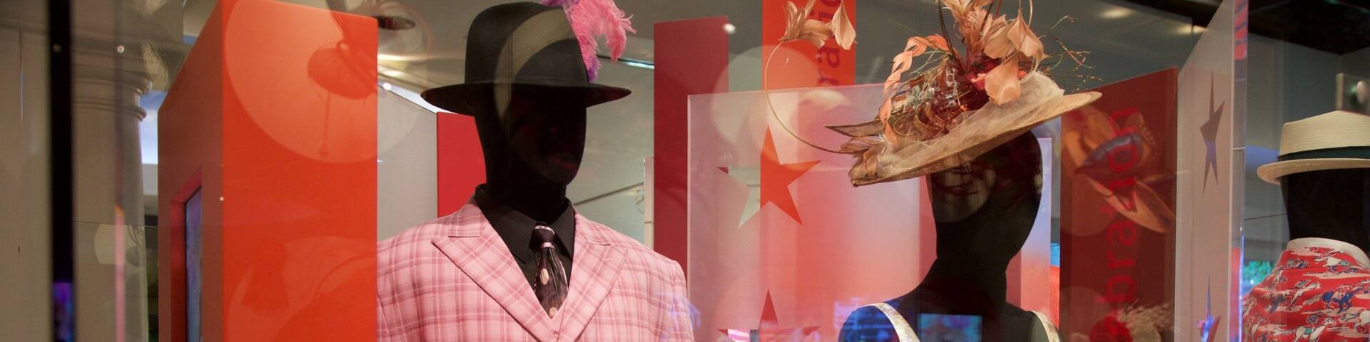 Maniquíes en un escaparate mostrando un traje rosa de cuadros y un vestido floral.