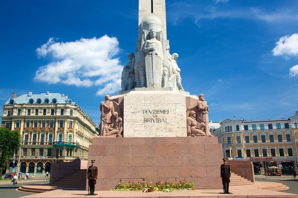 Un monumento con inscripciones, rodeado de edificios históricos y un cielo azul despejado.