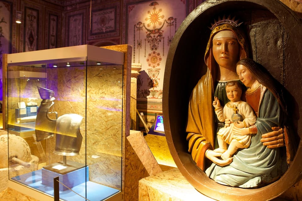 Una statua religiosa con un bambino, una teca con manufatti e un murale con motivi floreali.