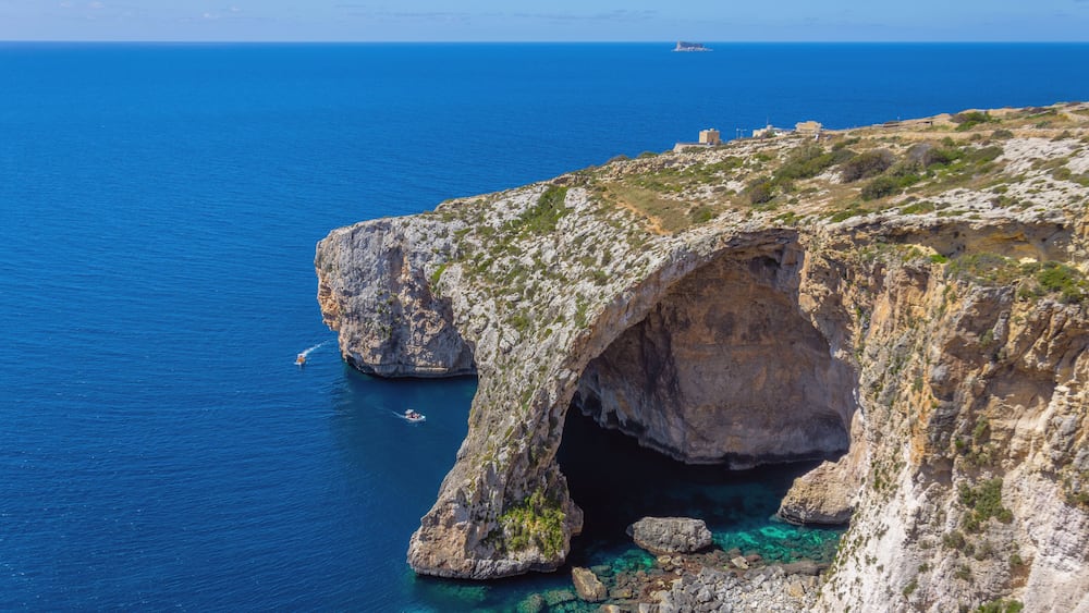 A coastal landscape with a prominent rock formation featuring a natural arch over clear blue waters.