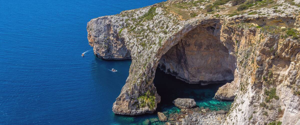 A coastal landscape with a prominent rock formation featuring a natural arch over clear blue waters.