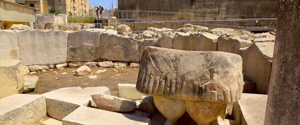 Ancient ruins with stone blocks and a large stone bull head sculpture.