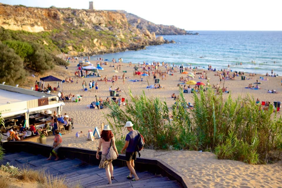 A crowded beach with people sunbathing and walking along the shore.