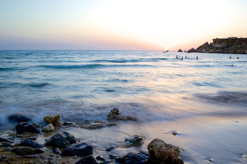 Una playa con rocas al frente y gente nadando en el agua.