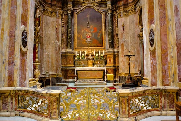 An ornate church interior with a central altar, gold decorations, and a crucifix.