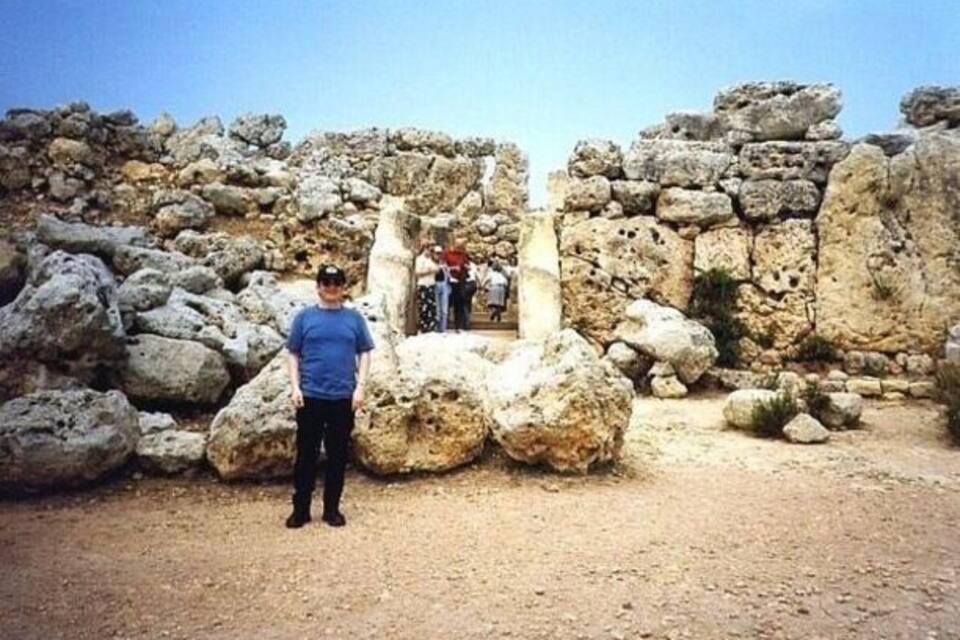 A person standing in front of ancient ruins with large rocks and stone structures.