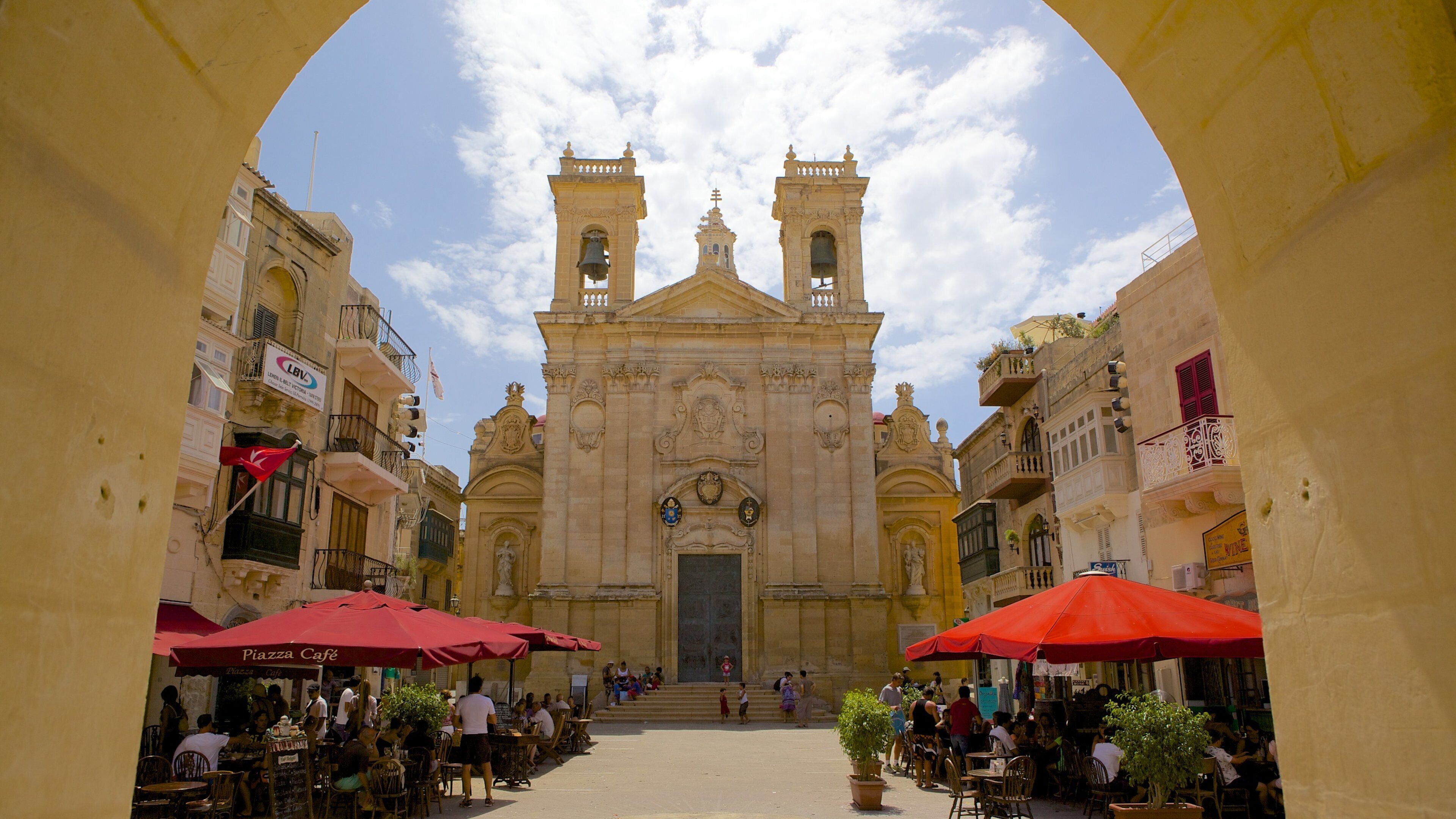 A historic church with two bell towers and a central dome, surrounded by cafes and outdoor seating.