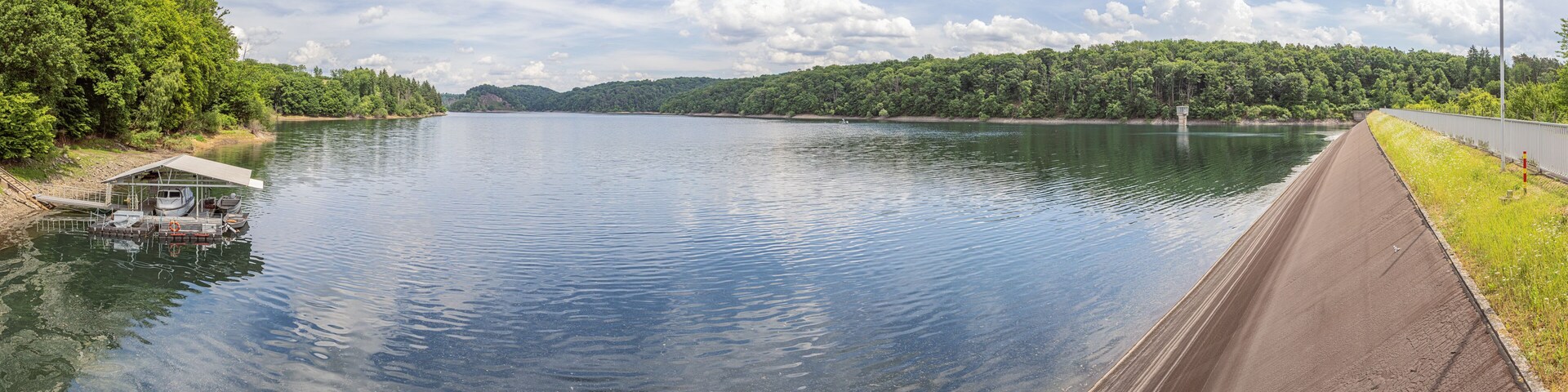 A calm lake with a dock, a dam, and a forested hillside.