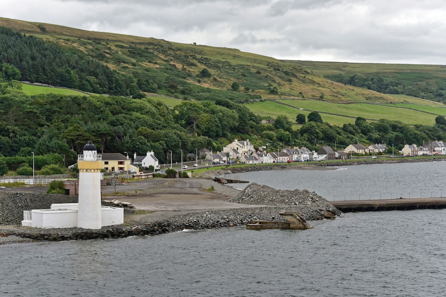 A coastal town with a lighthouse, houses, and a hill in the background.