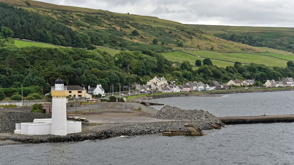 A coastal town with a lighthouse, houses, and a hill in the background.