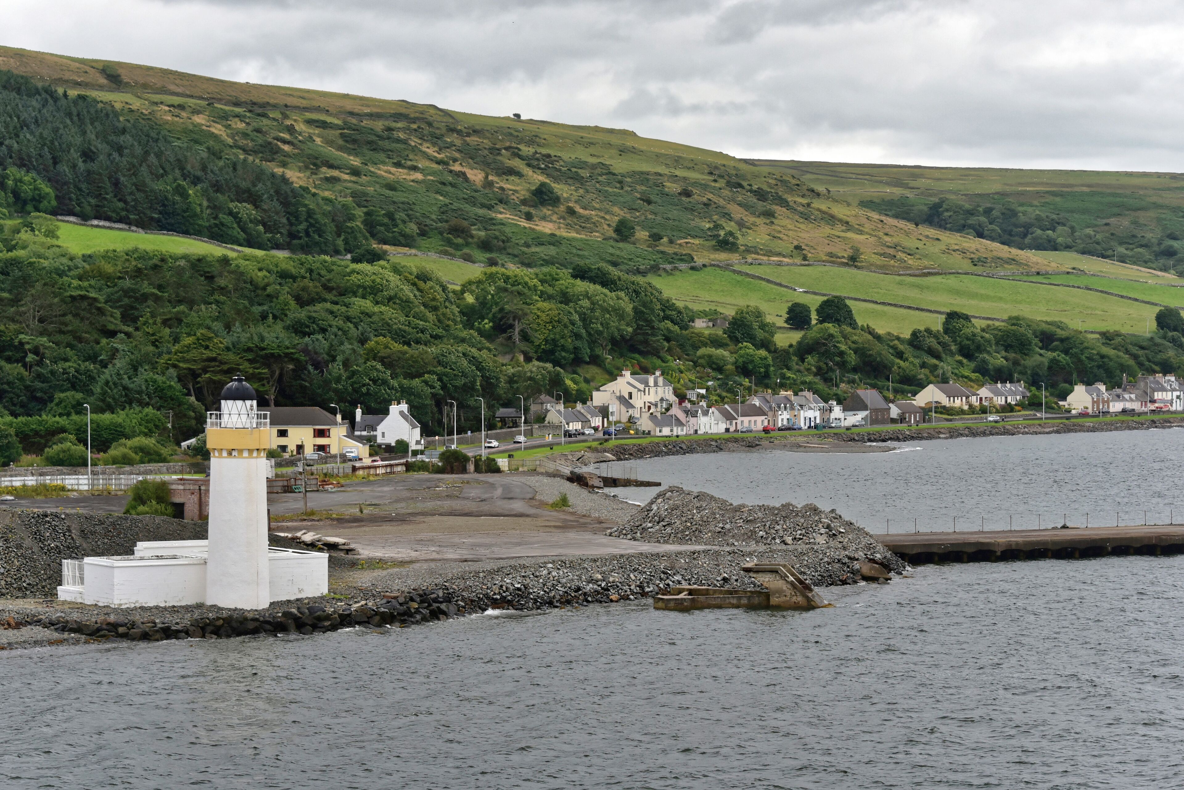 A coastal town with a lighthouse, houses, and a hill in the background.