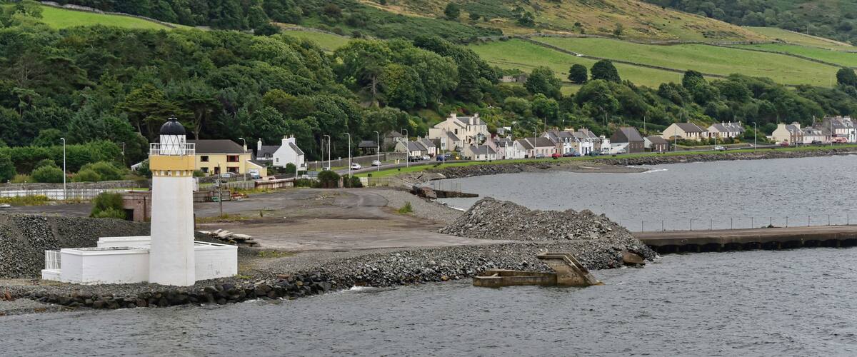 A coastal town with a lighthouse, houses, and a hill in the background.