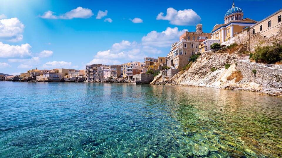 A coastal town with clear waters, historic buildings, and a prominent church with a blue dome.