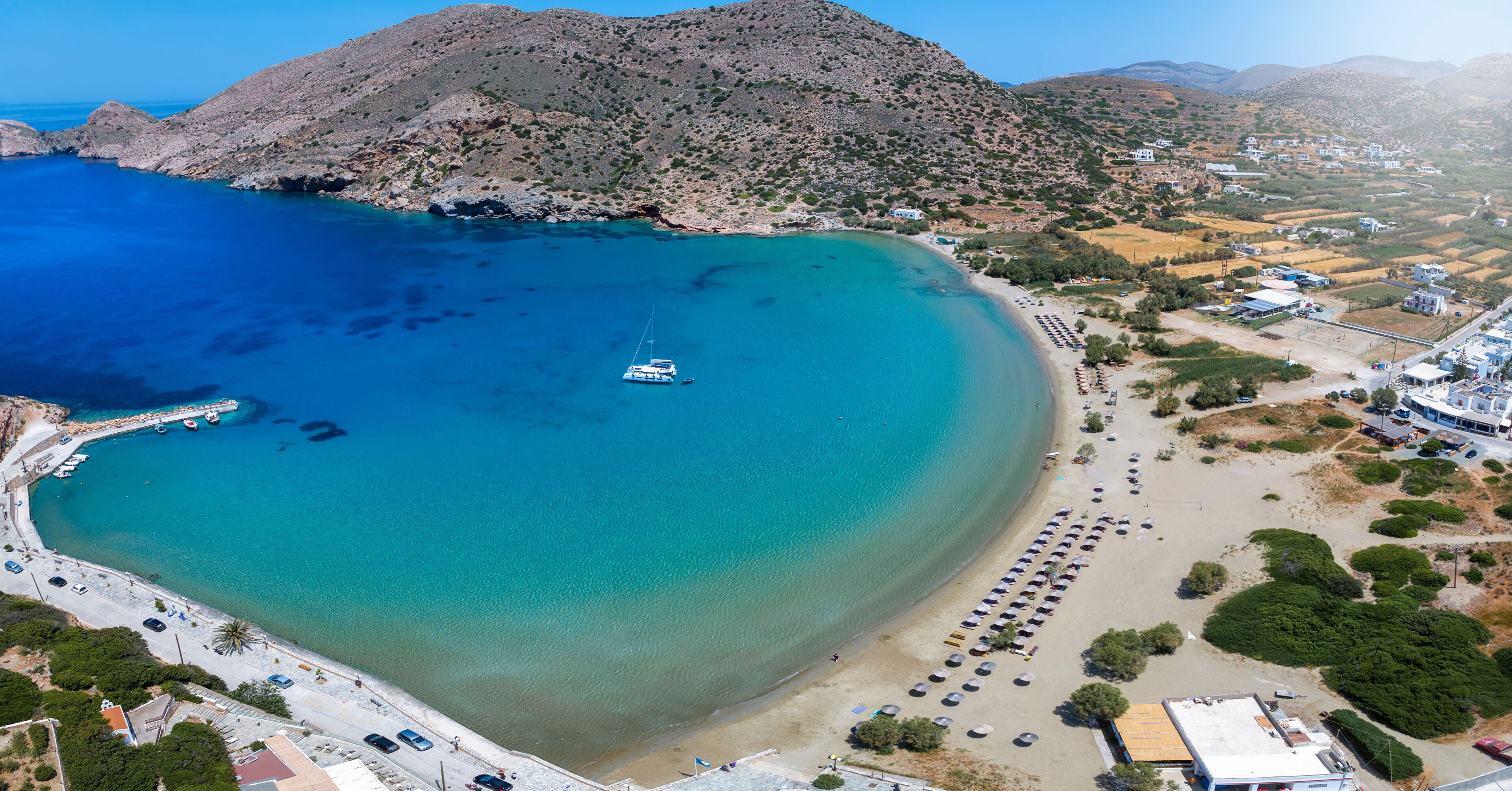 A coastal town with a clear blue bay, a white boat, and a beach with umbrellas.