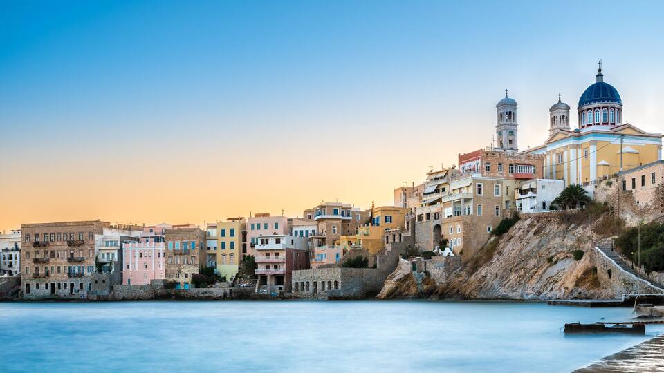 A coastal town with colorful buildings, a prominent church with domes, and a calm sea.