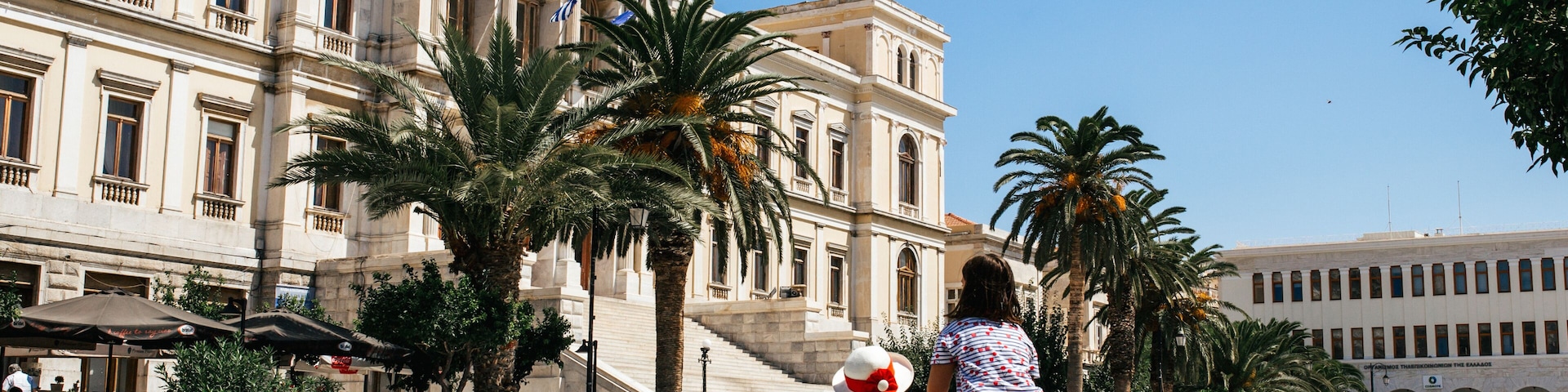 Um edifício histórico com arquitetura clássica, palmeiras e pombos em uma praça pública.