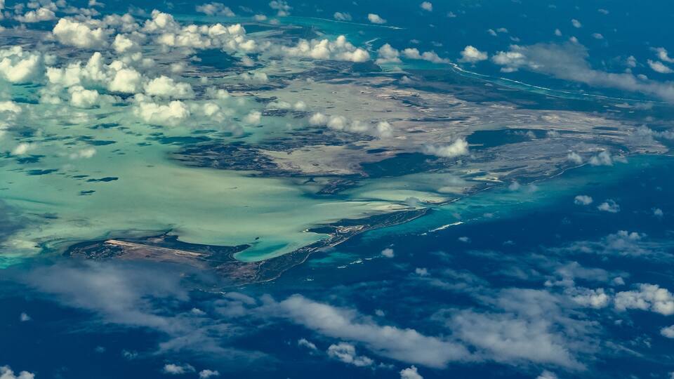 An aerial view of a coastal region with turquoise waters, scattered islands, and a mix of cloud cover.