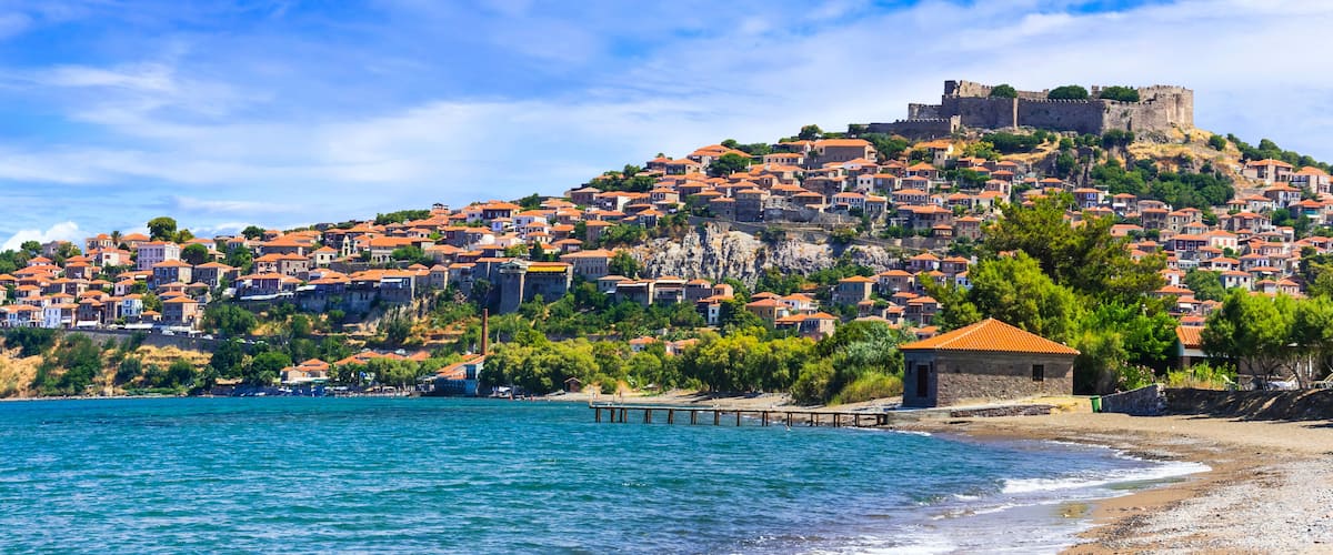 A coastal town with terracotta-roofed houses, a beach, and a castle on a hill.