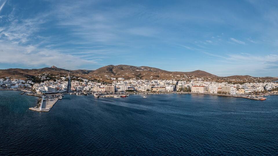 A coastal town with white buildings, a harbor, and mountains in the background.