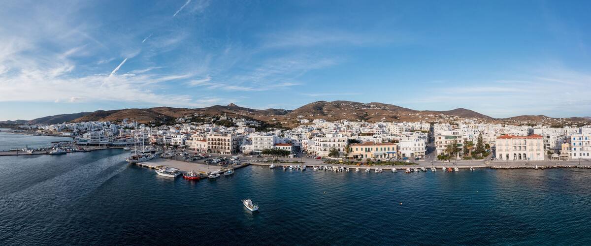 A coastal town with white buildings, a marina, and mountains in the background.