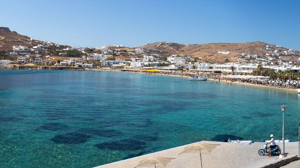 A coastal town with clear blue waters, a boat, and a hill in the background.