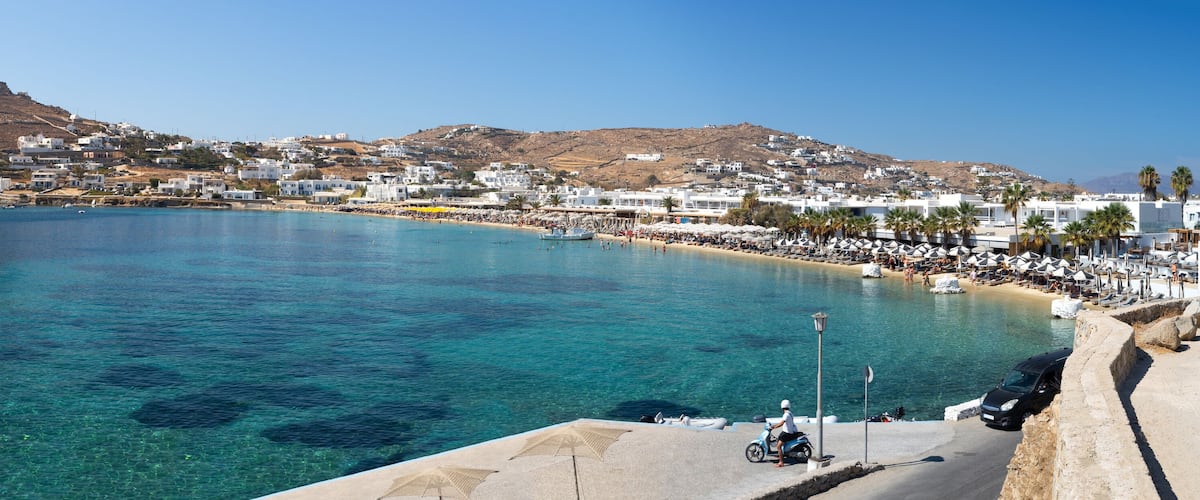 A coastal town with clear blue waters, a boat, and a hill in the background.