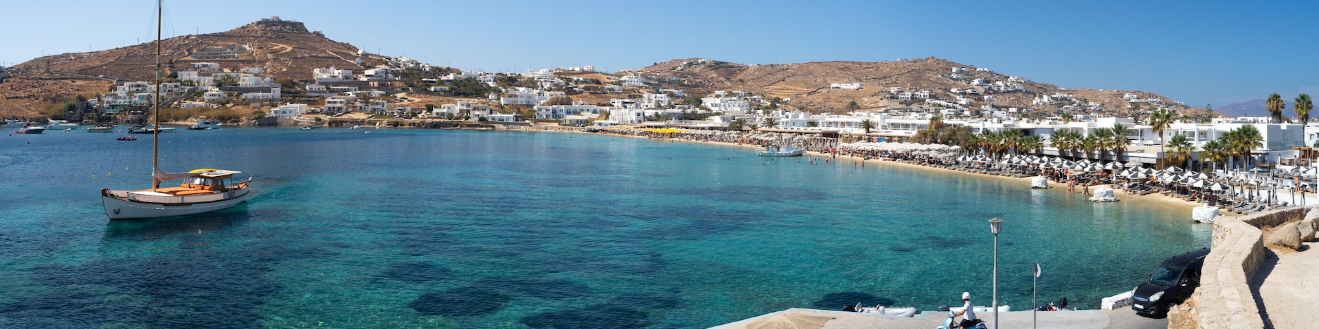 A coastal town with clear blue waters, a boat, and a hill in the background.