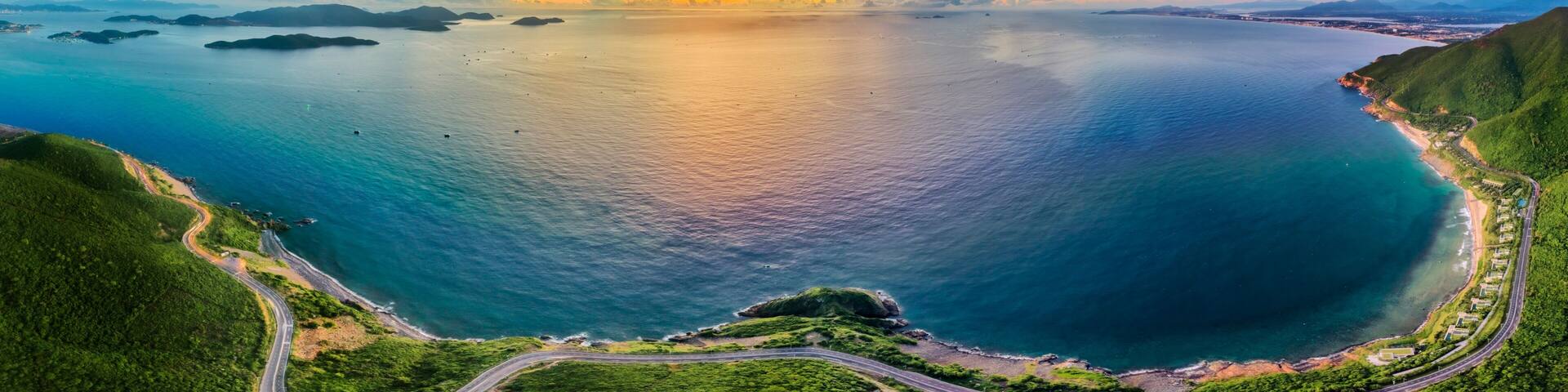 A coastal landscape with a winding road, green hills, and a large body of water.