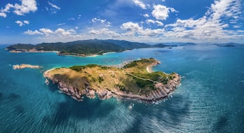 An aerial view of a coastal island with clear turquoise waters, green hills, and a small building on the shore.