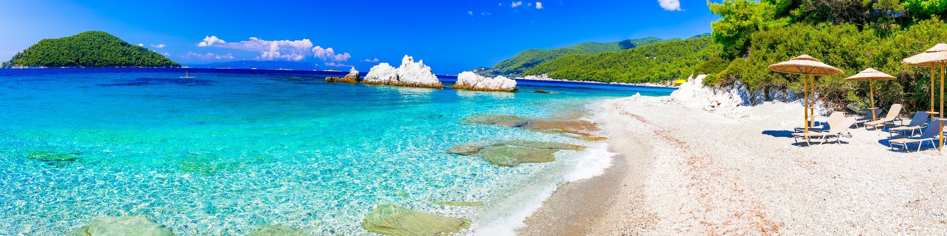 A beach with clear turquoise water, white sand, and rocky outcrops.