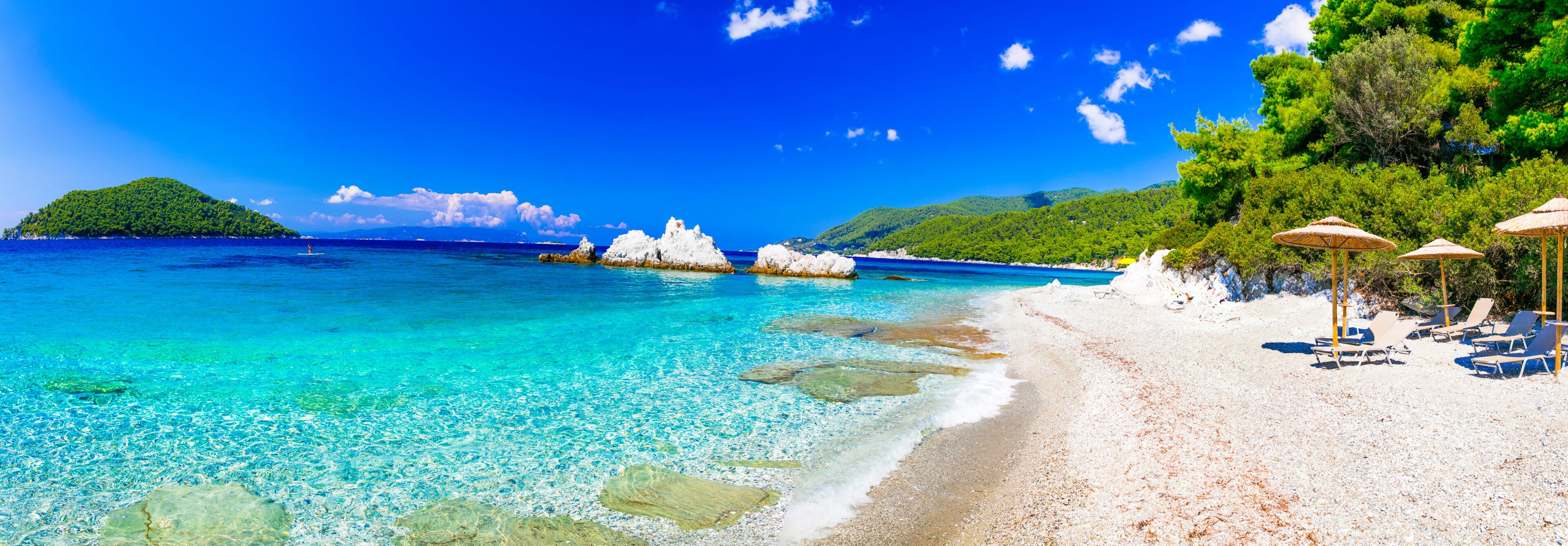 A beach with clear turquoise water, white sand, and rocky outcrops.