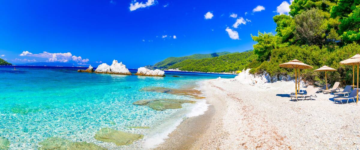 A beach with clear turquoise water, white sand, and rocky outcrops.