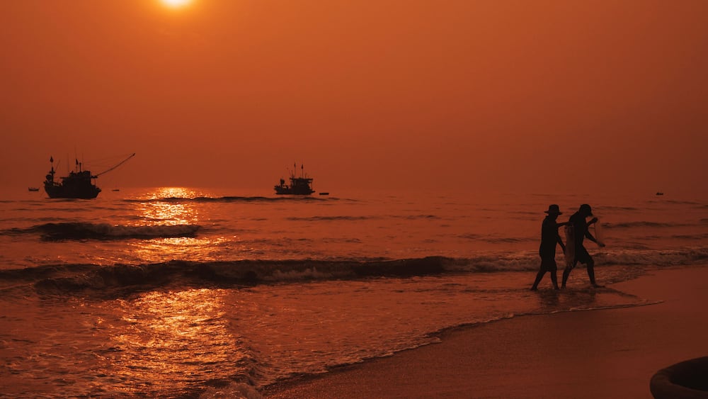Silhouettes of Vietnamese fishermen on the beach by sea with fishing boats in a fishing village in morning at sunrise in Vietnam