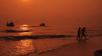 Un atardecer sobre el océano con dos personas caminando por la playa y varias embarcaciones en el agua.