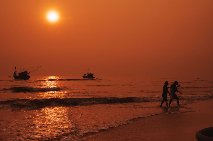 Silhouettes of Vietnamese fishermen on the beach by sea with fishing boats in a fishing village in morning at sunrise in Vietnam