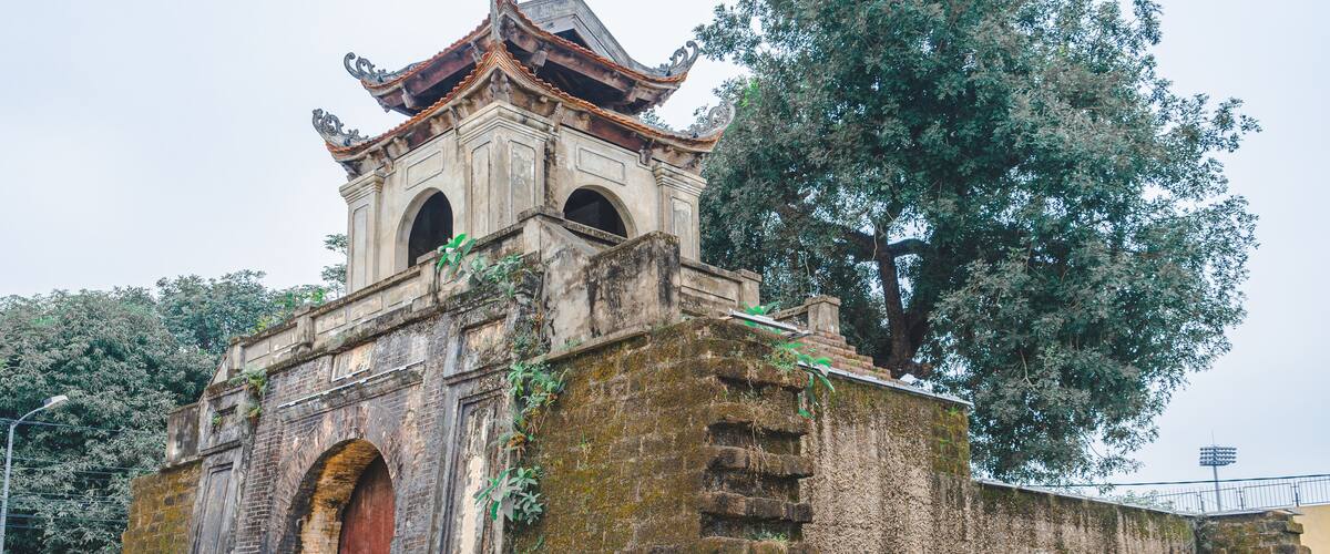 An ancient temple with a traditional roof, a large arched entrance, and a surrounding fence.