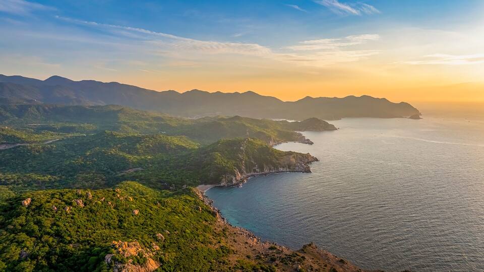 A coastal landscape with green hills and a calm sea during sunset.