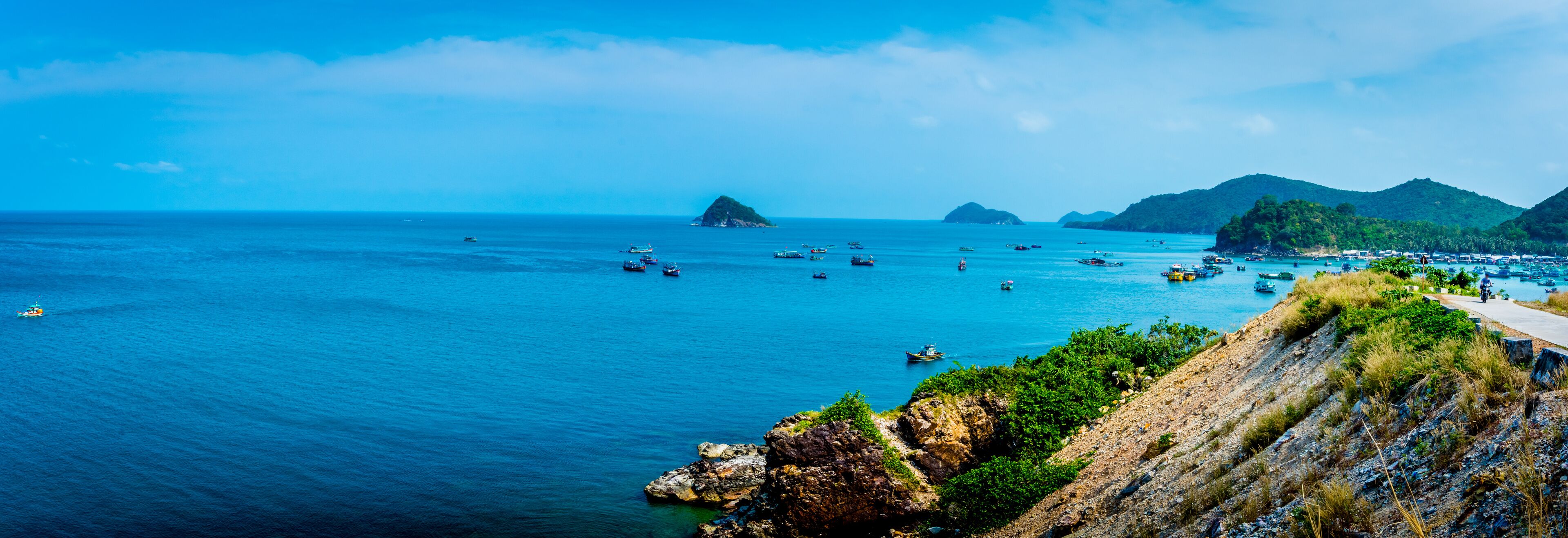 A coastal landscape with a clear blue sea, rocky cliffs, and several boats.