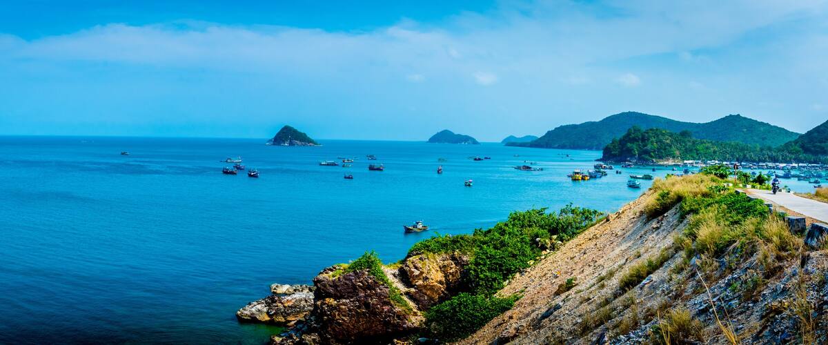 A coastal landscape with a clear blue sea, rocky cliffs, and several boats.