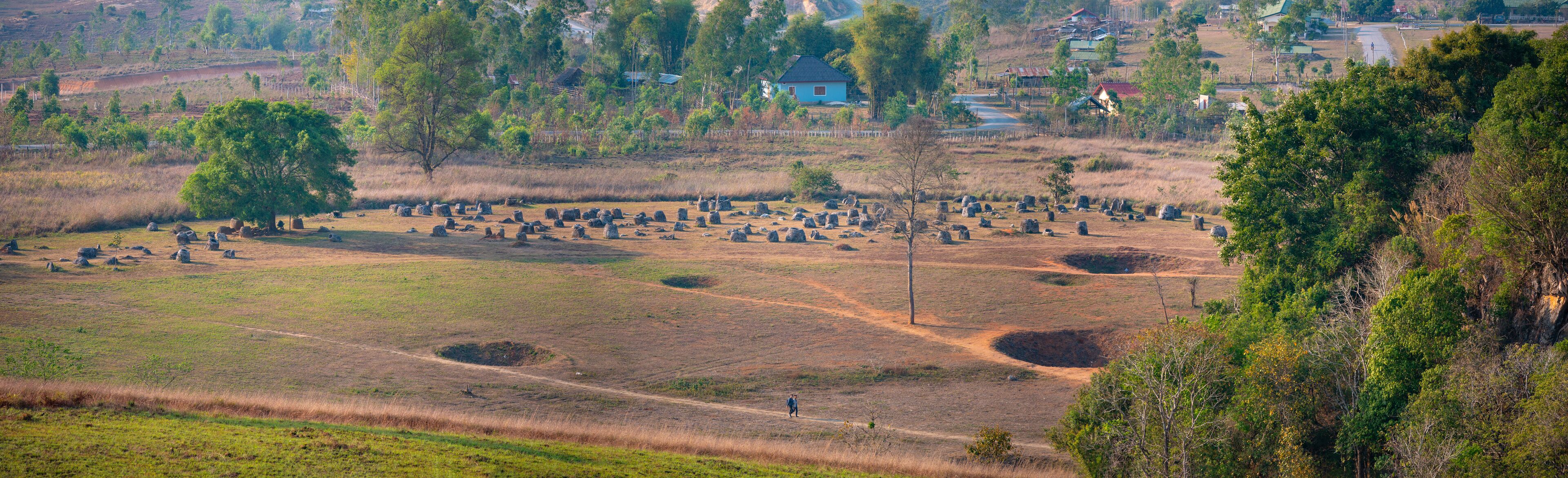 A rural landscape with scattered stone structures, a dirt path, and a blue house in the background.